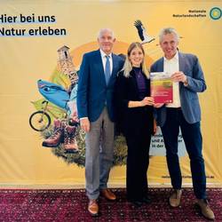 Prof. Dr. Hubert Job (links) und Dr. Lisa Majewski (mitte) von der Universität Würzburg überreichen den Leitfaden „Monitoring der Wertschöpfung durch Tourismus in den Nationalen Naturlandschaften“ an Peter Südbeck, Vorstandsvorsitzender Nationale Naturlandschaften e. V. © J. Wildefeld | NNL e.V. nnl uniwuerzburg 720x540